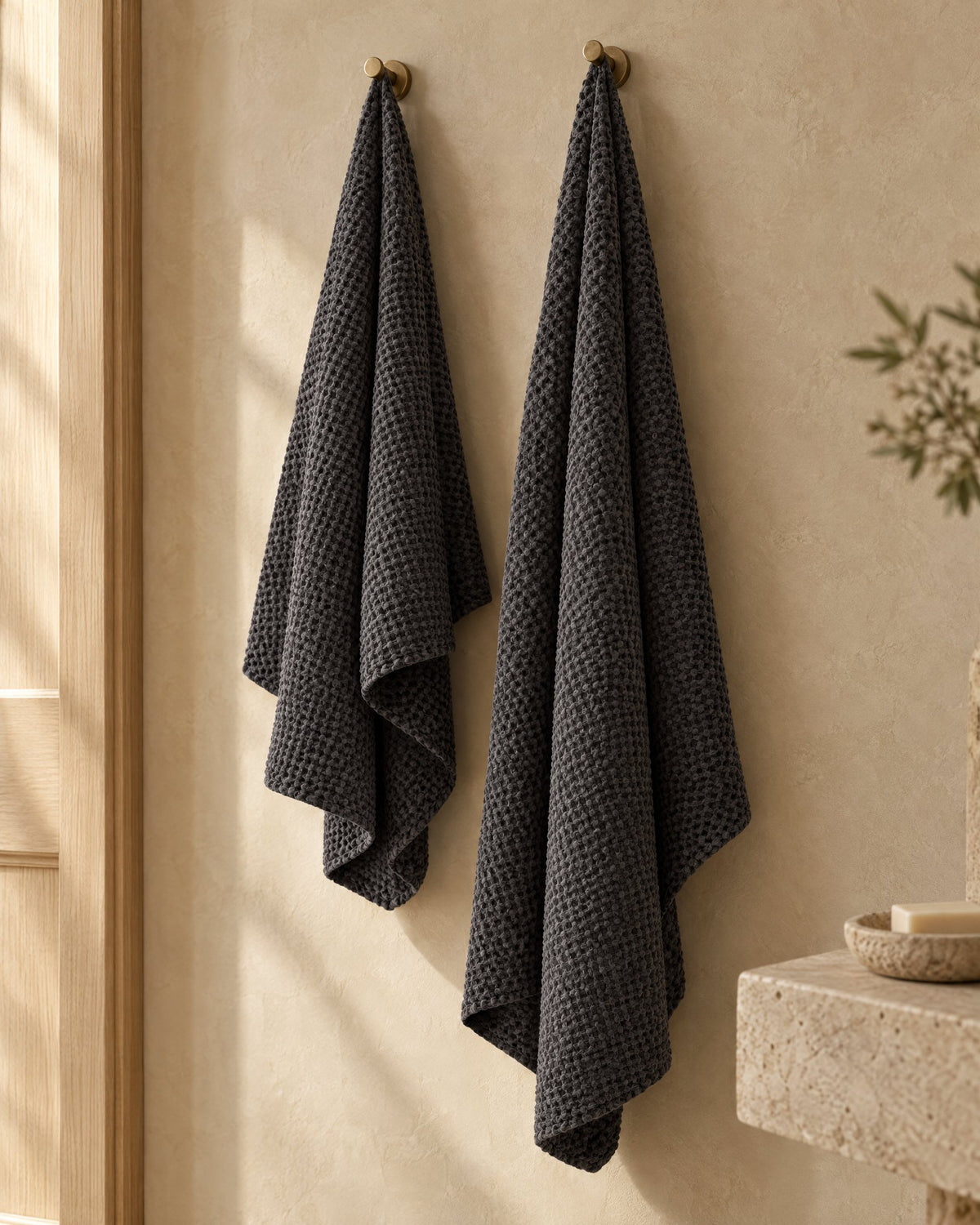 Two charcoal waffle bath towels hanging on brass hooks